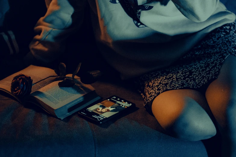 a woman sits in a chair with an open book and phone next to her