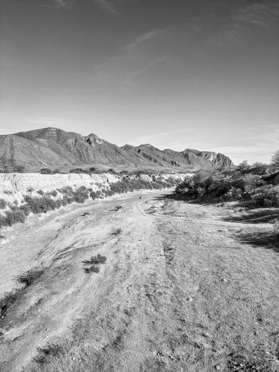 two people walking down a dirt road with mountains behind