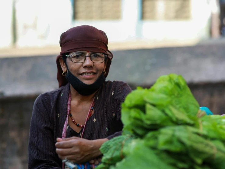 a woman holding a bunch of lettuce next to a pile of broccoli