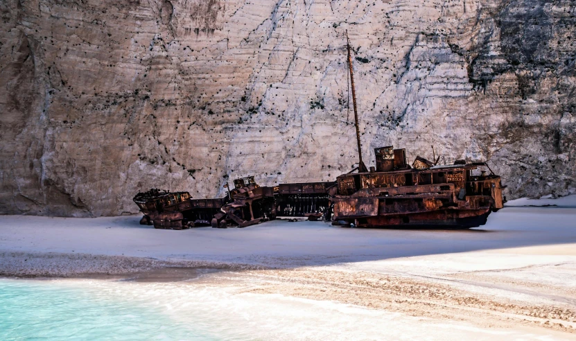 a rusted boat sits abandoned next to a mountain side