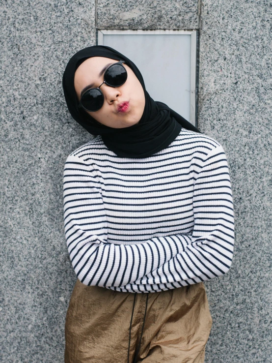 woman wearing sunglasses and hoodie, leaning against a wall