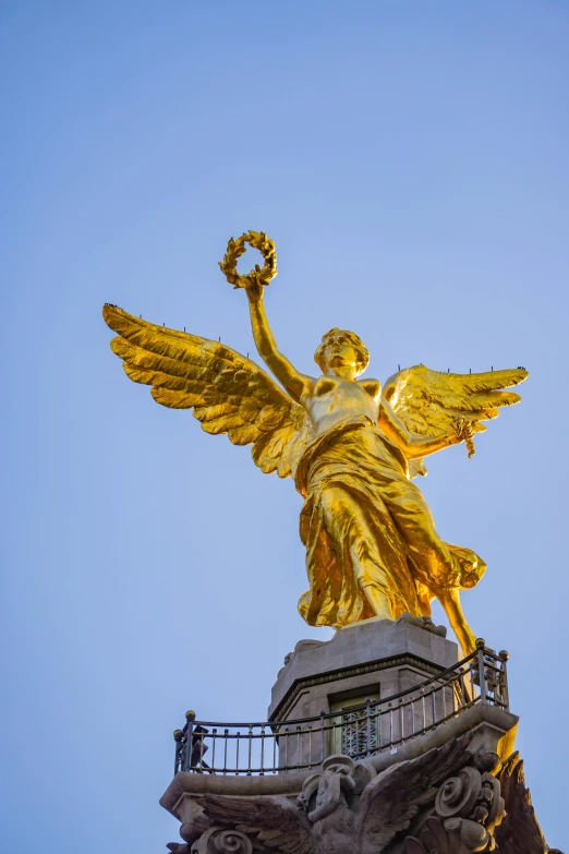 golden statue atop building with railing and blue sky