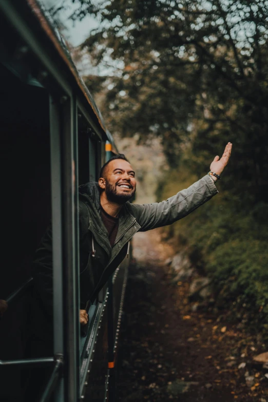 a man waving from the window of a train as he stands by the platform