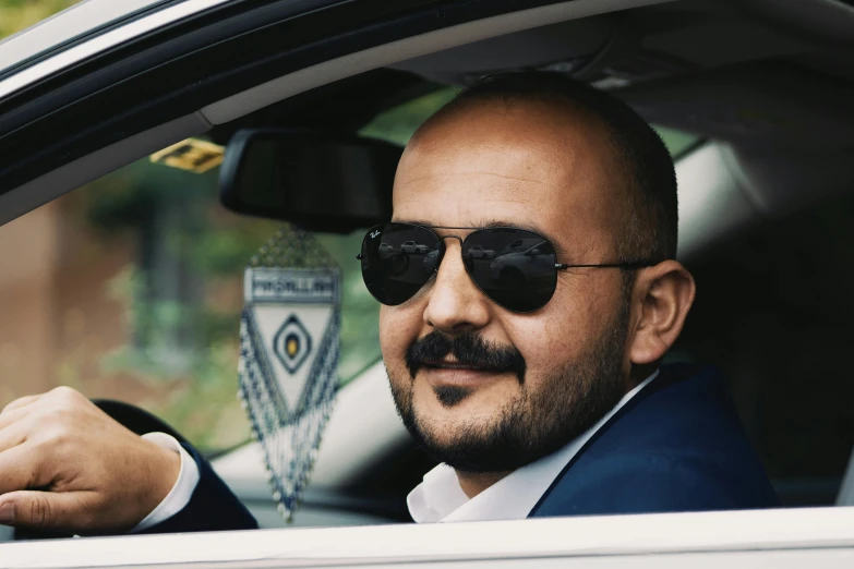 a man in a car smiling wearing black sunglasses