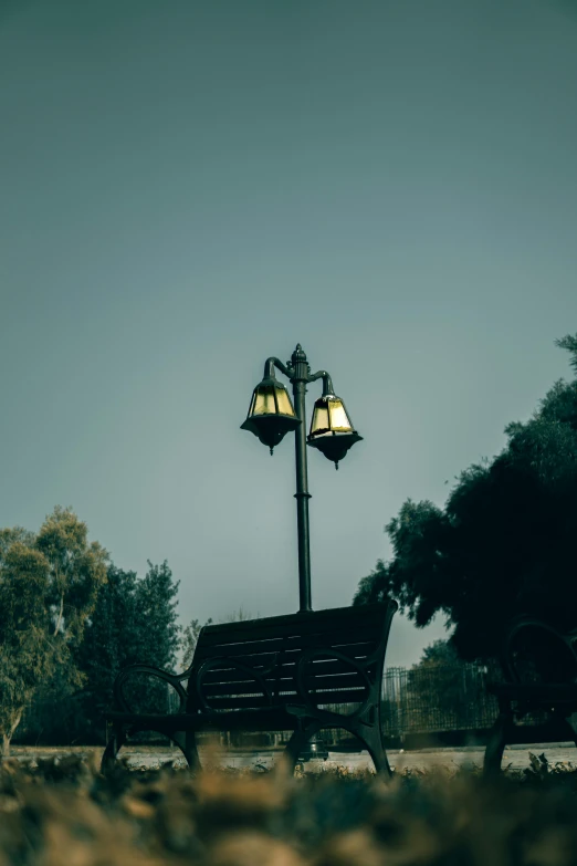 an empty park bench and lamp post with two lamps