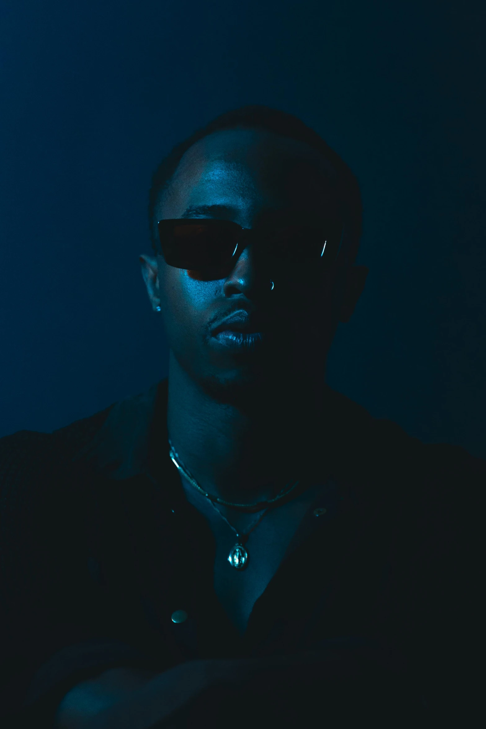 a person with shades on is wearing a black shirt and sitting in a dark room