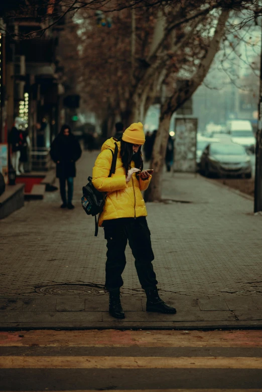 a man in yellow rain coat standing on sidewalk next to trees