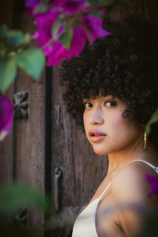 a girl with dark curly hair stands by flowers