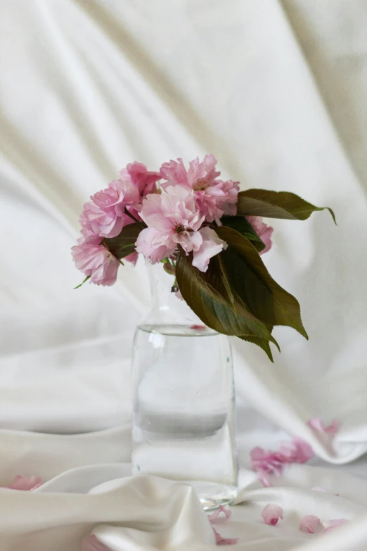 pink flowers sit in a vase on a white silk