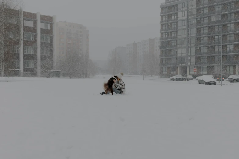 a man and woman kissing in the snow with buildings in background