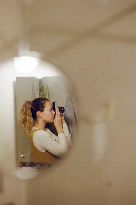 a woman holding a camera looks at her reflection in the mirror