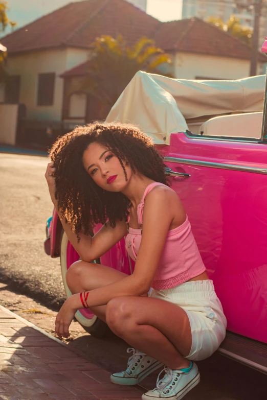 a woman with long curly hair sitting against a pink car