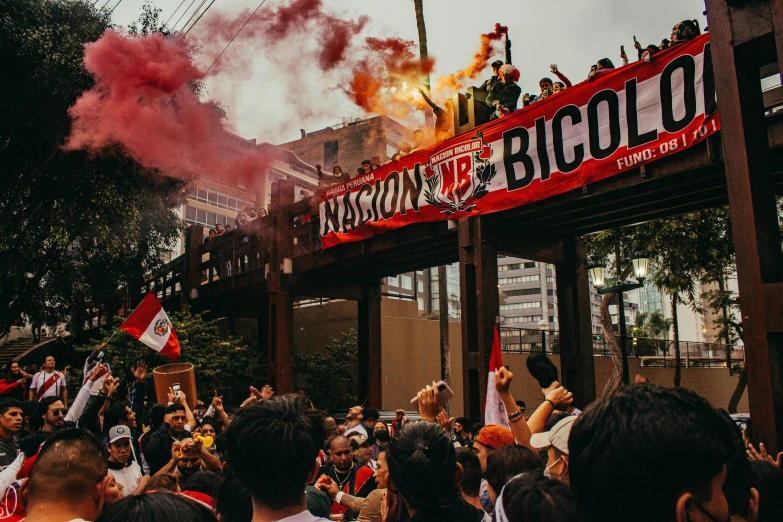 people gathered in front of a red banner as smoke and stream of red smoke rise from a building
