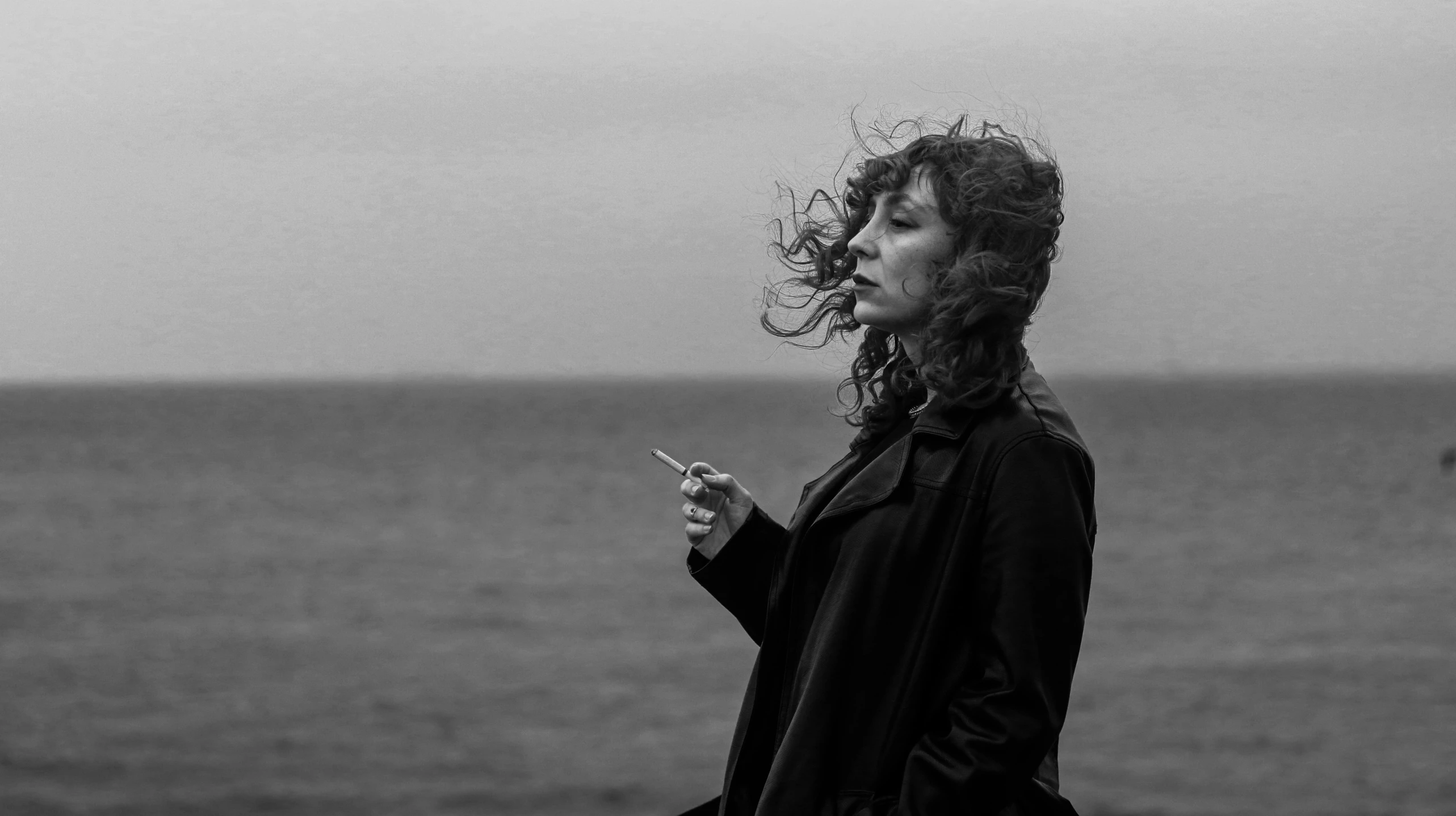 a woman standing by the ocean while holding a cell phone