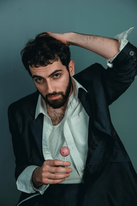 a man with a beard, wearing a suit jacket and holding his finger up in front of his face