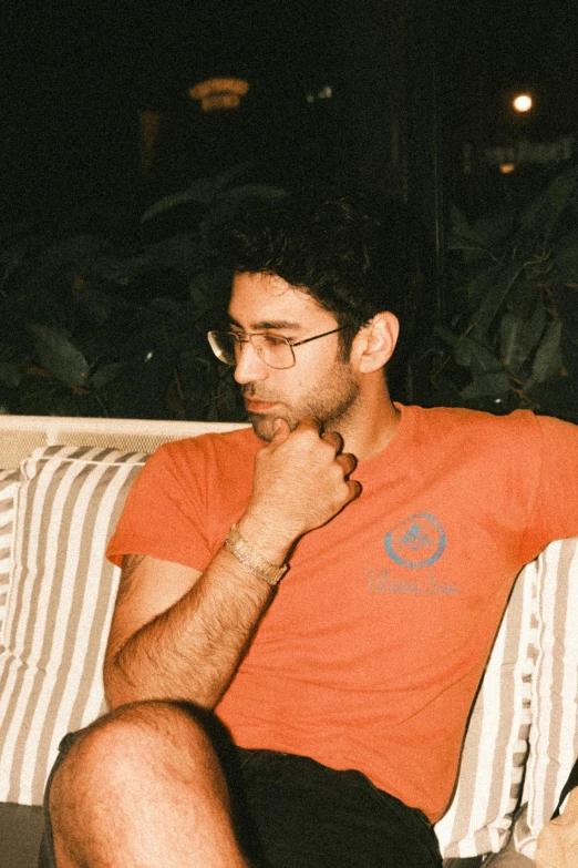 a man wearing an orange shirt, sitting on a striped pillow