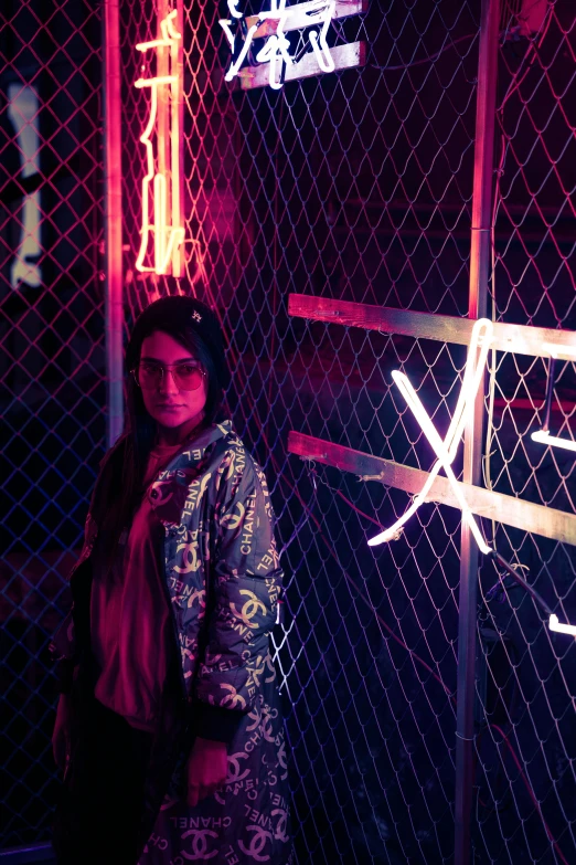 a girl is standing beside a fence with neon lights on it