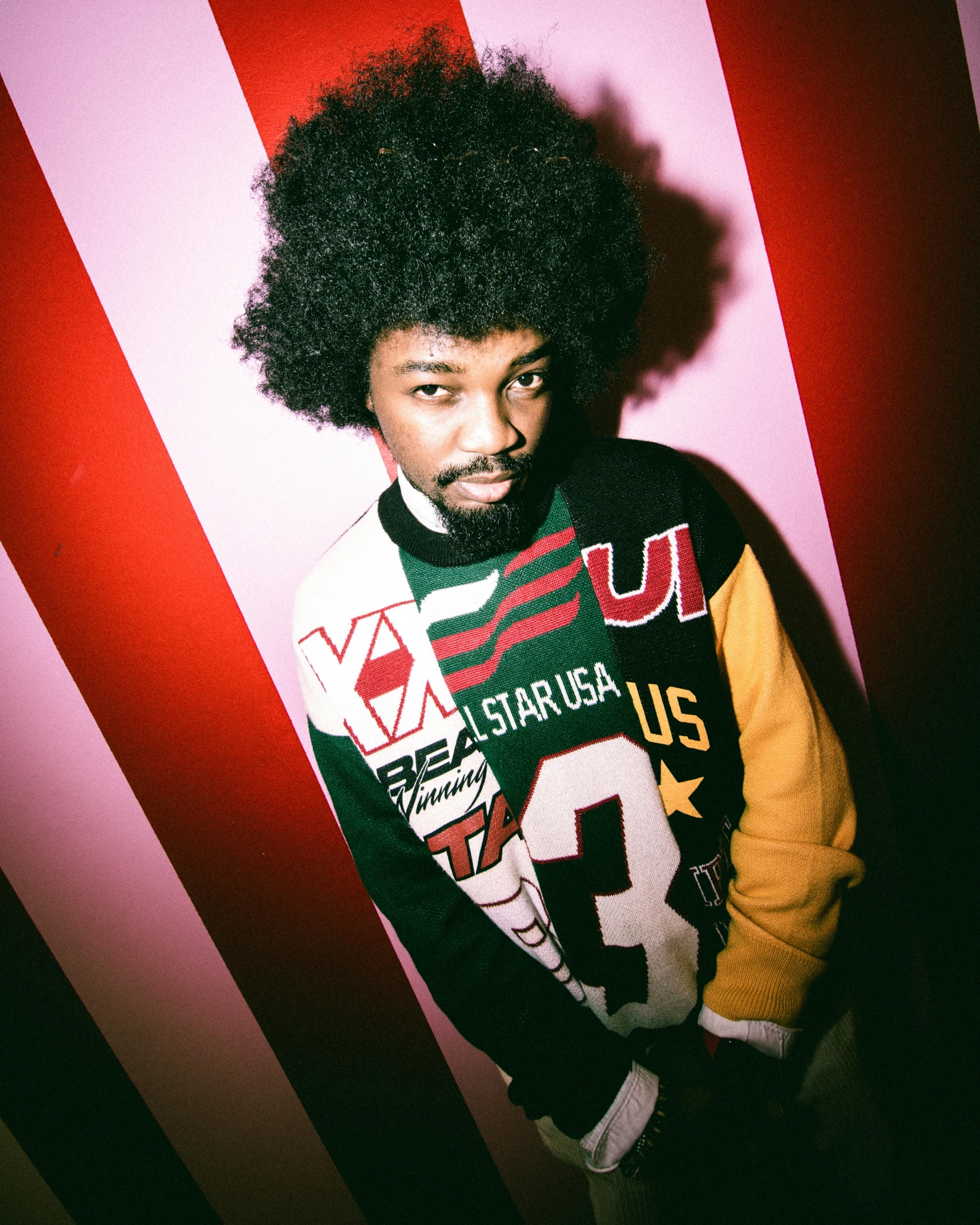 a young man with an afro is standing in front of a wall