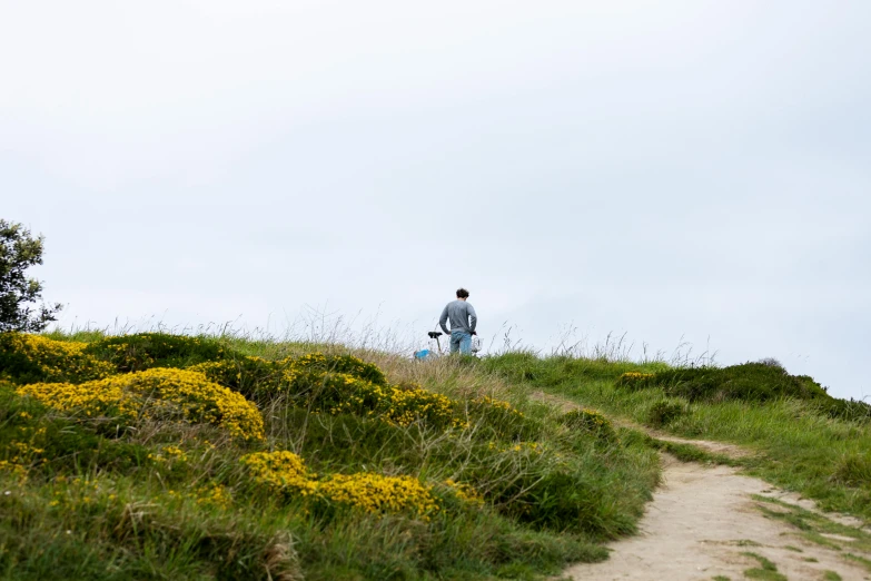 a man stands atop of a grassy hill with a backpack