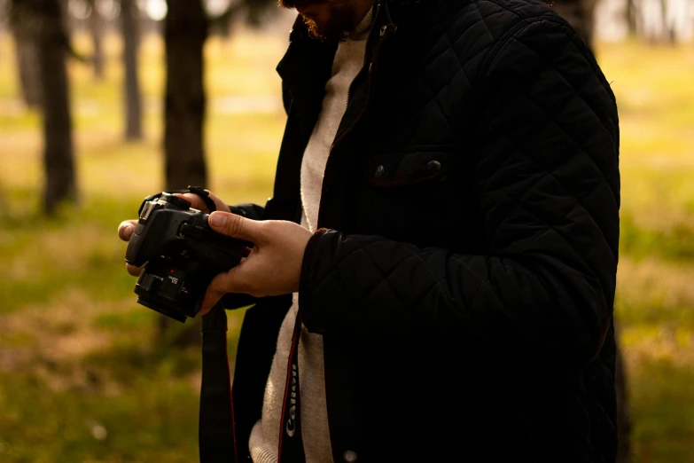 a man with a camera in his hand and trees behind him