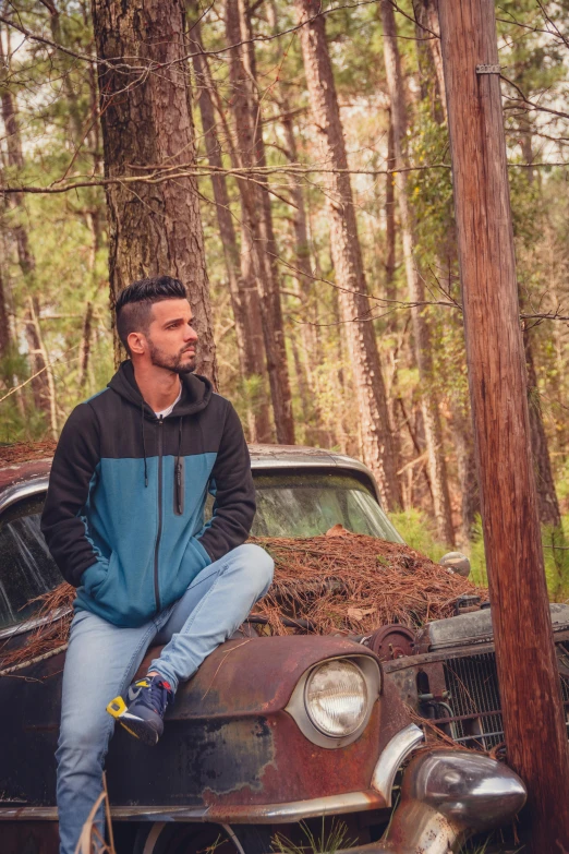 the man is sitting on an old car in the forest