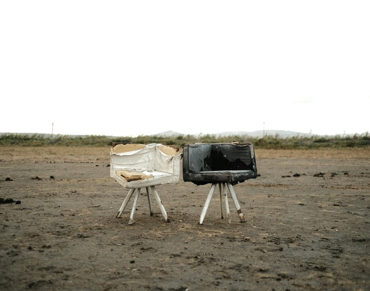 a small white chair in a dirt field near a television set