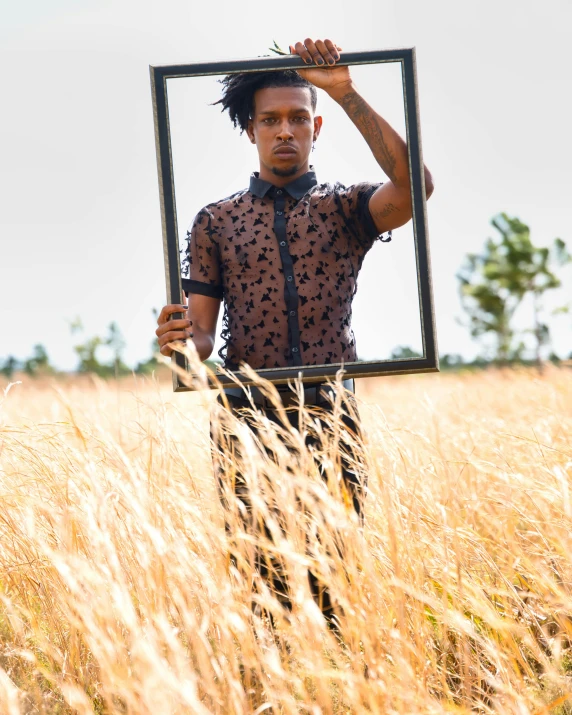 a man holding up a picture frame in an empty field