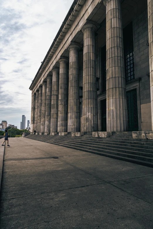 a woman walking down a street past some stone columns