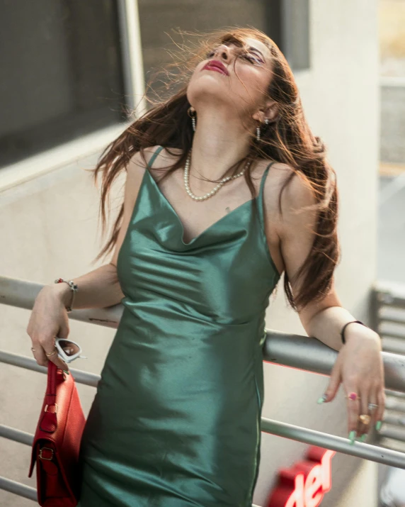 a woman poses in front of a fence while holding a handbag