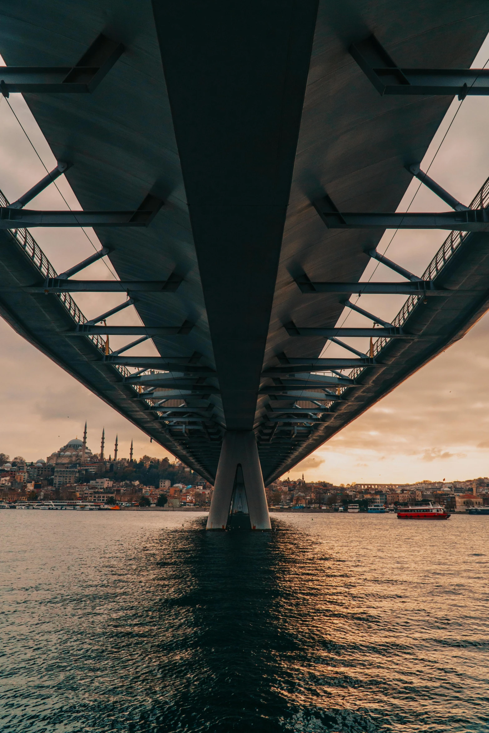 sunsets reflect off the water beneath an elevated suspension bridge