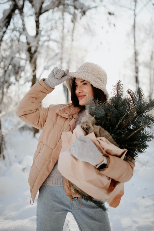 a woman walking through snow with a bag and a small pine tree