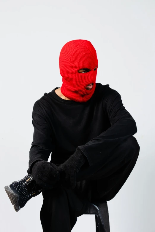 the man is sitting down with his legs crossed and a mask on