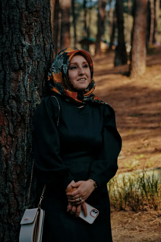 a beautiful young woman leaning against a tree with her head scarf on