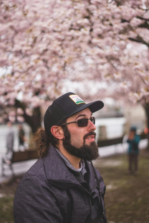 man in baseball hat and sunglasses standing under a tree with blossoms