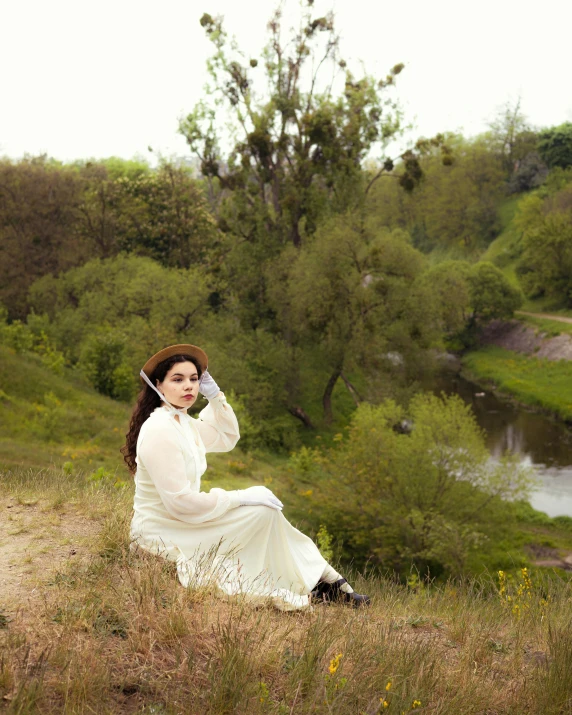 woman in white dress on grassy hill with pond and trees