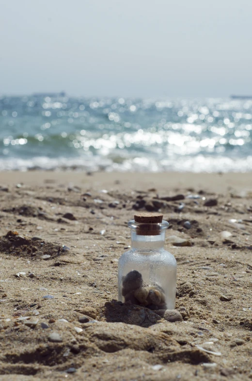 a bottle filled with two rocks sitting in the sand