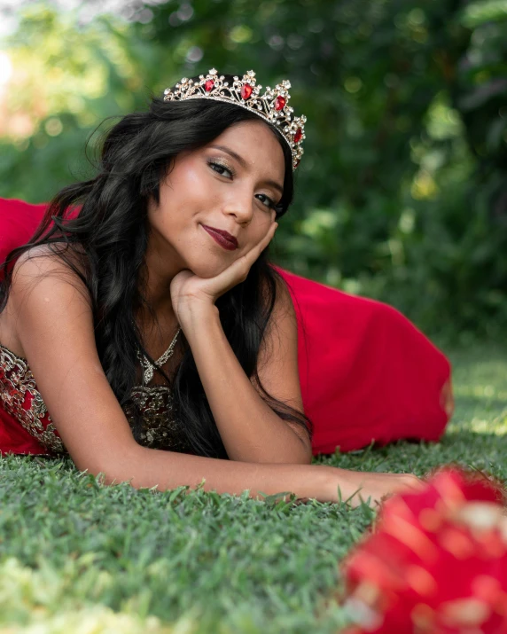 a woman laying on the ground with her arm around her chest wearing a red dress and a tiara