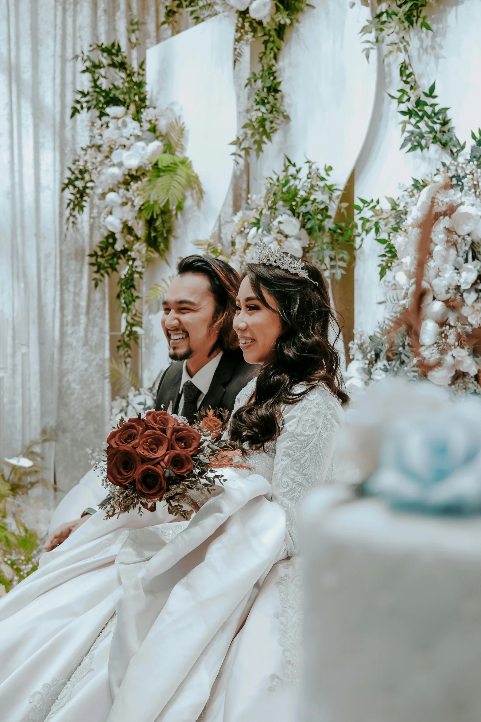 a couple posing for a po while sitting next to each other in front of a decorated wedding cake