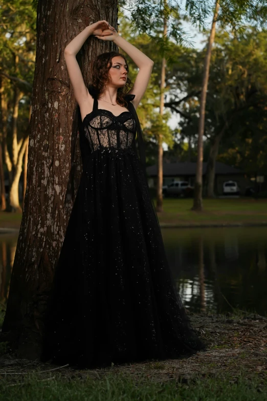 a woman in a black dress poses against a tree