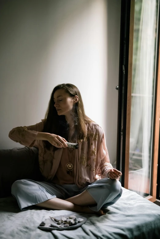 a woman in a pink shirt sitting on a bed brushing her long hair