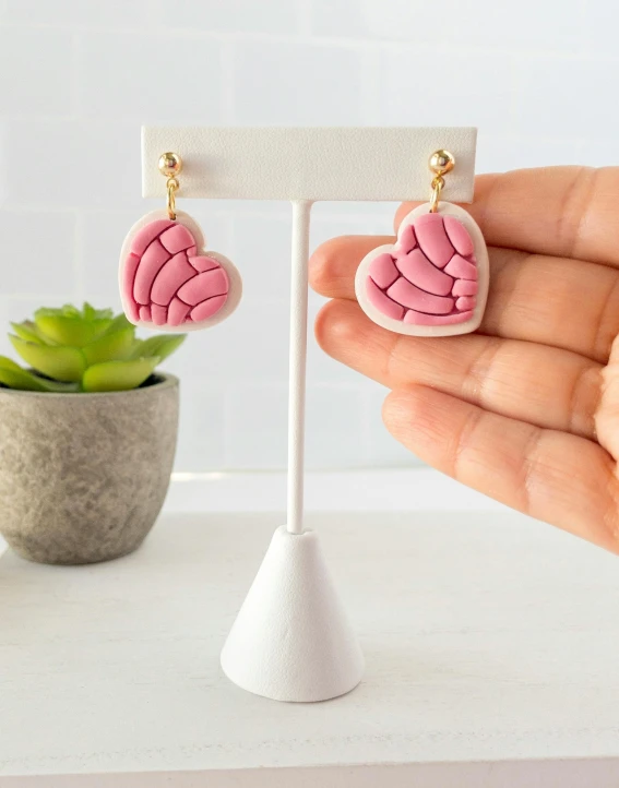 a pair of pink heart shaped earrings on top of a white stand