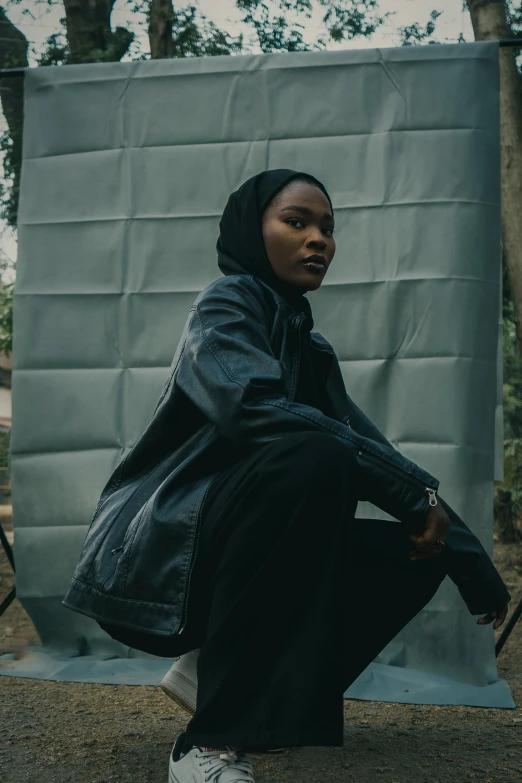 a woman is sitting against a gray wall