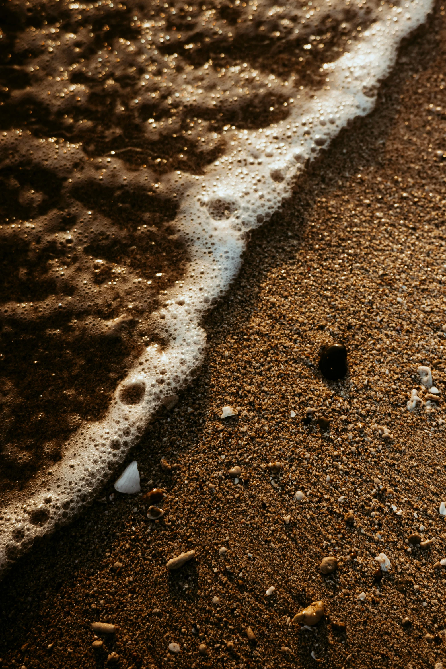 a wet sandy beach area next to a wave and white foam