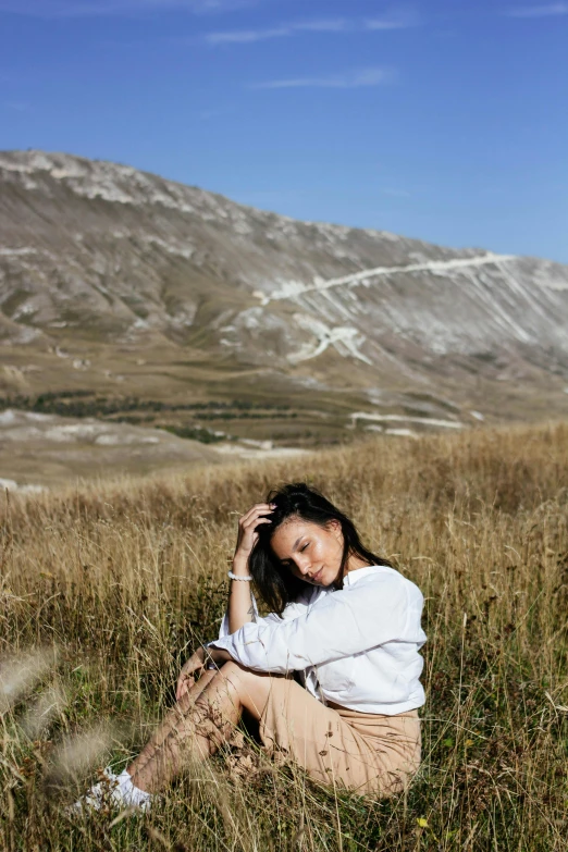 a woman sitting in a field with mountains behind her