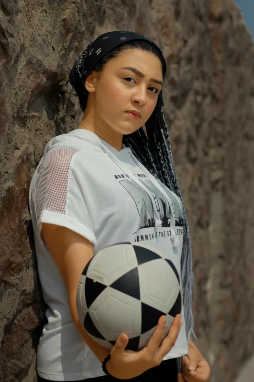 a young lady holding a soccer ball against a rock