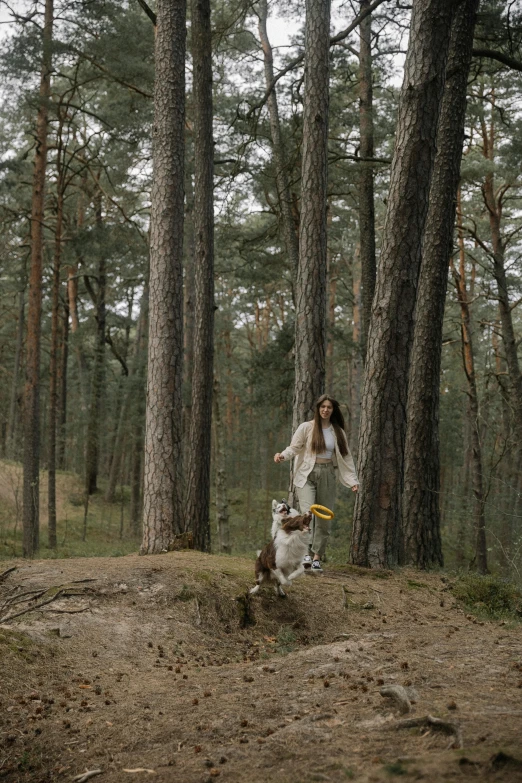 a woman in white is standing among trees and a dog