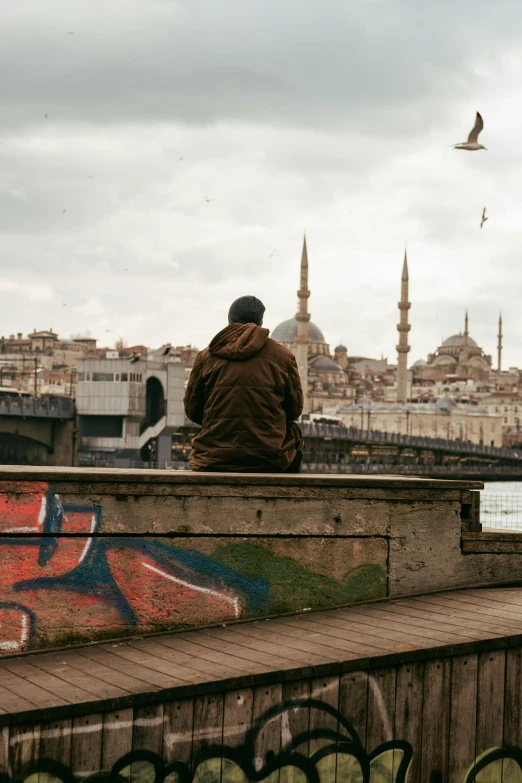 man sitting on cement wall next to building with bird flying above