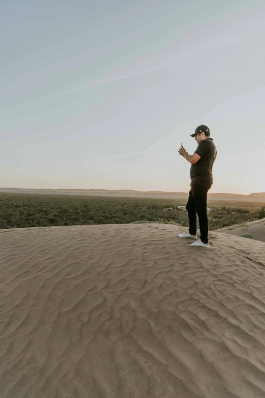 man on top of large dune using cell phone