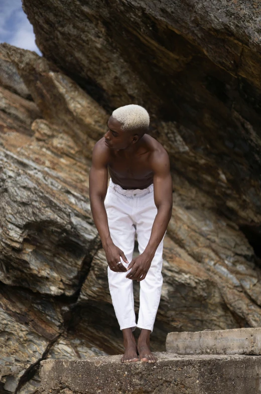 man wearing white clothes sitting on the rocks in front of a rock face