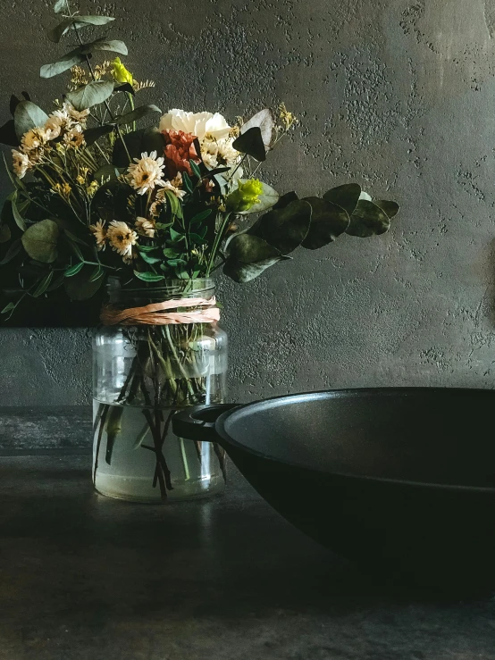 a mason jar of flowers next to a frying pan